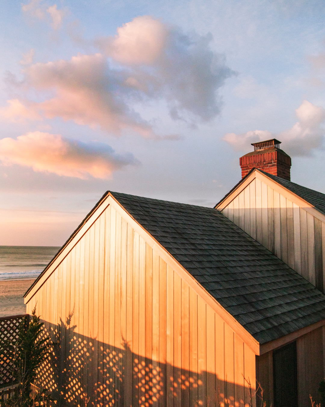 Rooftops of a house with a chimney at sunset, sky with pink and orange clouds.